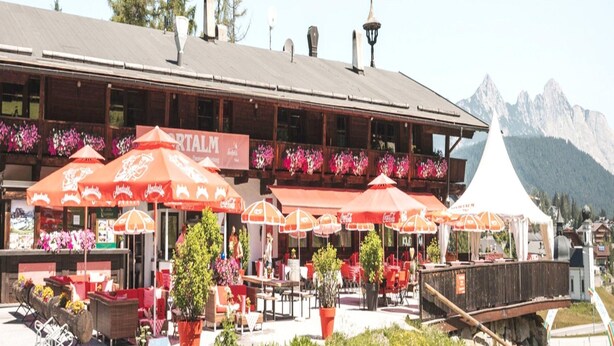 Restaurante con terraza, sombrillas rojas y montañas al fondo.