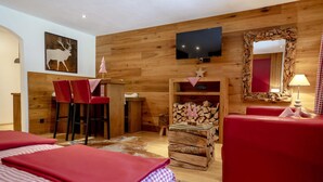 Habitación de hotel con paredes de madera, un televisor sobre un mueble de madera, un sofá rojo, un escritorio con sillas y una cama con ropa de cama roja.