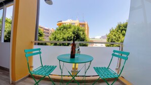 A balcony with a green metal table and chairs, a bottle, and a glass.
