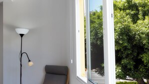 A corner room with a chair, a floor lamp, and a window with a view of greenery.