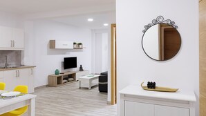 A modern kitchen with white cabinets, a dining area with yellow chairs, and a living space with a TV and sofa.