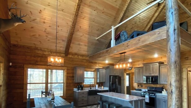 A cozy cabin interior with a dining area, kitchen, and a loft bedroom. - Custom Log Cabin in French Lick (French Lick)