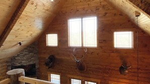 A log cabin interior with a stone fireplace, wooden beams, and three windows. - Custom Log Cabin in French Lick (French Lick)
