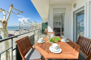 A balcony with a wooden table set for two, chairs, and a small potted plant. - Apartment in Roses With Waterfront Views (Roses)