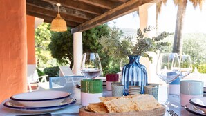 Una mesa dispuesta con platos, vasos, un florero con follaje y un cuenco de pan plano.