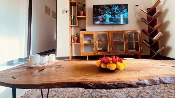 Una habitación con una mesa de madera, un tapete estampado, un televisor y una estantería.