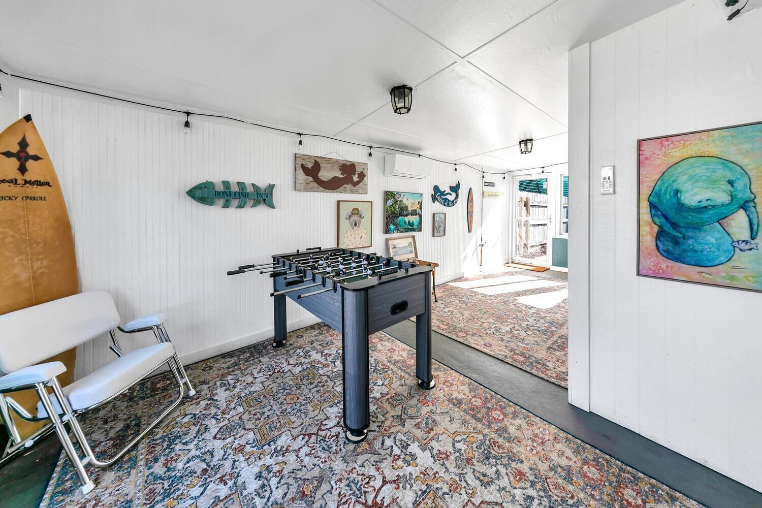 Una habitación con una mesa de fútbol de mesa, una silla, un tapete estampado y varias decoraciones en la pared, incluyendo peces y una pintura de una ballena.