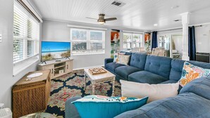 A living room with a large blue sofa, a TV, and a view of the beach through the windows.