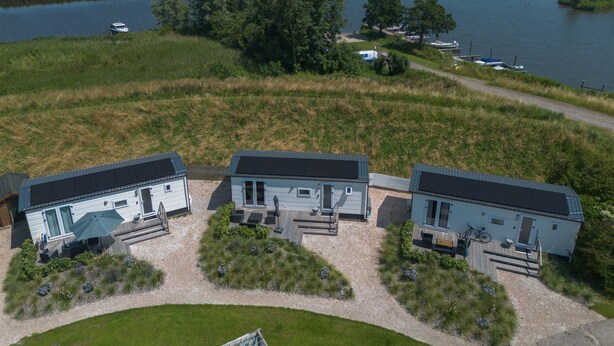 A modern, three-story residential building with a flat roof, located near a body of water. - New chalet 1 on the edge of the Wadden Sea and Amstelmeer with private terrace! (Anna Paulowna)