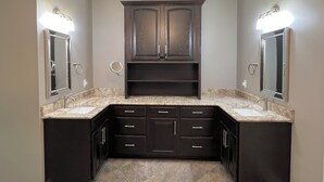 A modern bathroom with dark cabinetry, a marble countertop, and dual wall-mounted mirrors with lighting.