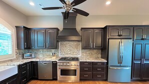 A modern kitchen with dark cabinetry, stainless steel appliances, a gas stove, and a ceiling fan.
