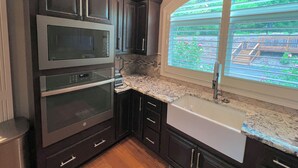 A kitchen with dark cabinetry, a built-in oven, a microwave, and a window with a view of a garden.