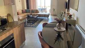 A modern living room with a sofa, a dining table, and a kitchen area with a stove. - Haut Standing apartment in a prime location: just 5 minutes from the beach, with sea views (Mahdia)