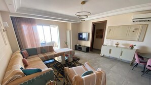 A modern living room with a large sofa, a coffee table, and a TV. There is a dining area with a table and chairs. - Haut Standing apartment in a prime location: just 5 minutes from the beach, with sea views (Mahdia)