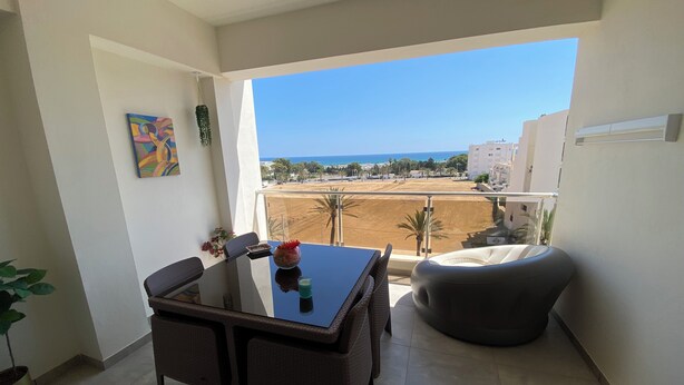 A balcony with a dining table, chairs, a vase with flowers, and a view of the beach and buildings. - Haut Standing apartment in a prime location: just 5 minutes from the beach, with sea views (Mahdia)