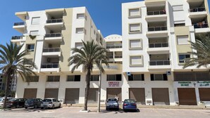 A multi-story building with balconies, parked cars, and palm trees. - Haut Standing apartment in a prime location: just 5 minutes from the beach, with sea views (Mahdia)