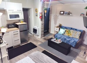 A compact living space with a kitchenette, a sofa with a floral pattern, a coffee table, and a television. - Charming Jawn in Fabulous Fishtown — W/D, AC, Private Patio & Fast WiFi (Philadelphia)
