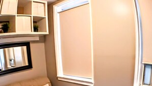 A room with a beige sofa, a small white table, and a window with blinds. - Charming Jawn in Fabulous Fishtown — W/D, AC, Private Patio & Fast WiFi (Philadelphia)