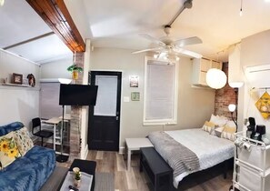 A compact room with a bed, a desk, a sofa, a ceiling fan, and a TV mounted on the wall. - Charming Jawn in Fabulous Fishtown — W/D, AC, Private Patio & Fast WiFi (Philadelphia)