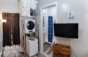 A compact room with a washing machine, a television, and a shower area. - Charming Jawn in Fabulous Fishtown — W/D, AC, Private Patio & Fast WiFi (Philadelphia)