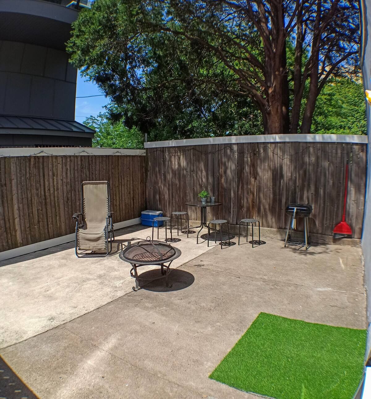Un patio à l’arrière de la maison, avec un barbecue, une chaise, une table et un petit coin jardin.