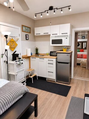 A compact kitchen with white cabinets, a microwave, a refrigerator, and a small dining area with a bench. - Charming Jawn in Fabulous Fishtown — W/D, AC, Private Patio & Fast WiFi (Philadelphia)