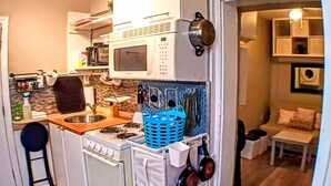A compact kitchen with a stove, microwave, and hanging pots. - Charming Jawn in Fabulous Fishtown — W/D, AC, Private Patio & Fast WiFi (Philadelphia)