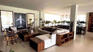 A spacious living room with a large sofa, a coffee table, and a dining area with a table and chairs. There are several potted plants and a large painting on the wall. - Casa El Encanto Priv Rooftop With Tub Best Loc (El Tezal)