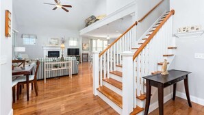 Un vaste espace de vie agrémenté d’un escalier en bois, d’un coin repas et d’une cuisine située à l’arrière-plan.