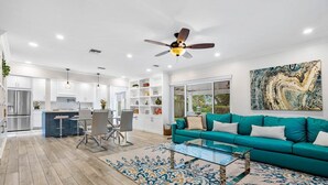 A modern kitchen with white cabinetry, a dining area with a glass table, and a teal sofa in a living room. - Downtown Las Olas Paradise + HOT TUB (Fort Lauderdale)