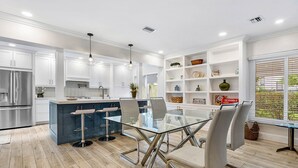 A modern kitchen with white cabinets, a central island with stools, and a glass dining table. - Downtown Las Olas Paradise + HOT TUB (Fort Lauderdale)