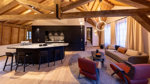Amplia sala de estar con un gran techo de madera, una isla central con taburetes de bar, un sofá y una mesa de centro.