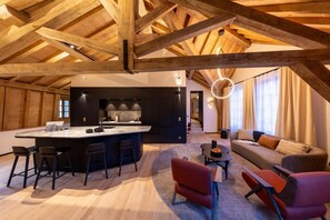 A spacious living area with a large wooden ceiling, a central island with bar stools, a sofa, and a coffee table. - Les Suites by Cave Vauban - Suite Bô (Dijon)