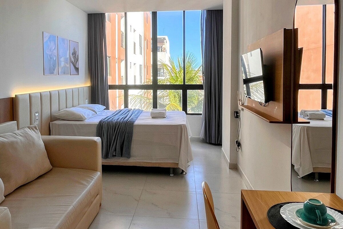 A hotel room with a bed, a sofa, a dining table, and a TV.