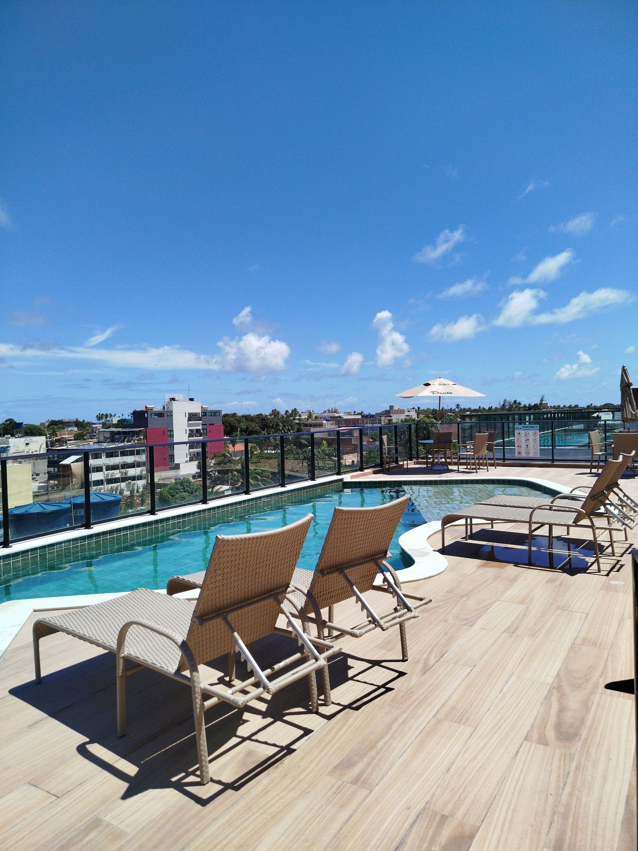 Área de piscina en la azotea con sillones de descanso y vistas a la ciudad.