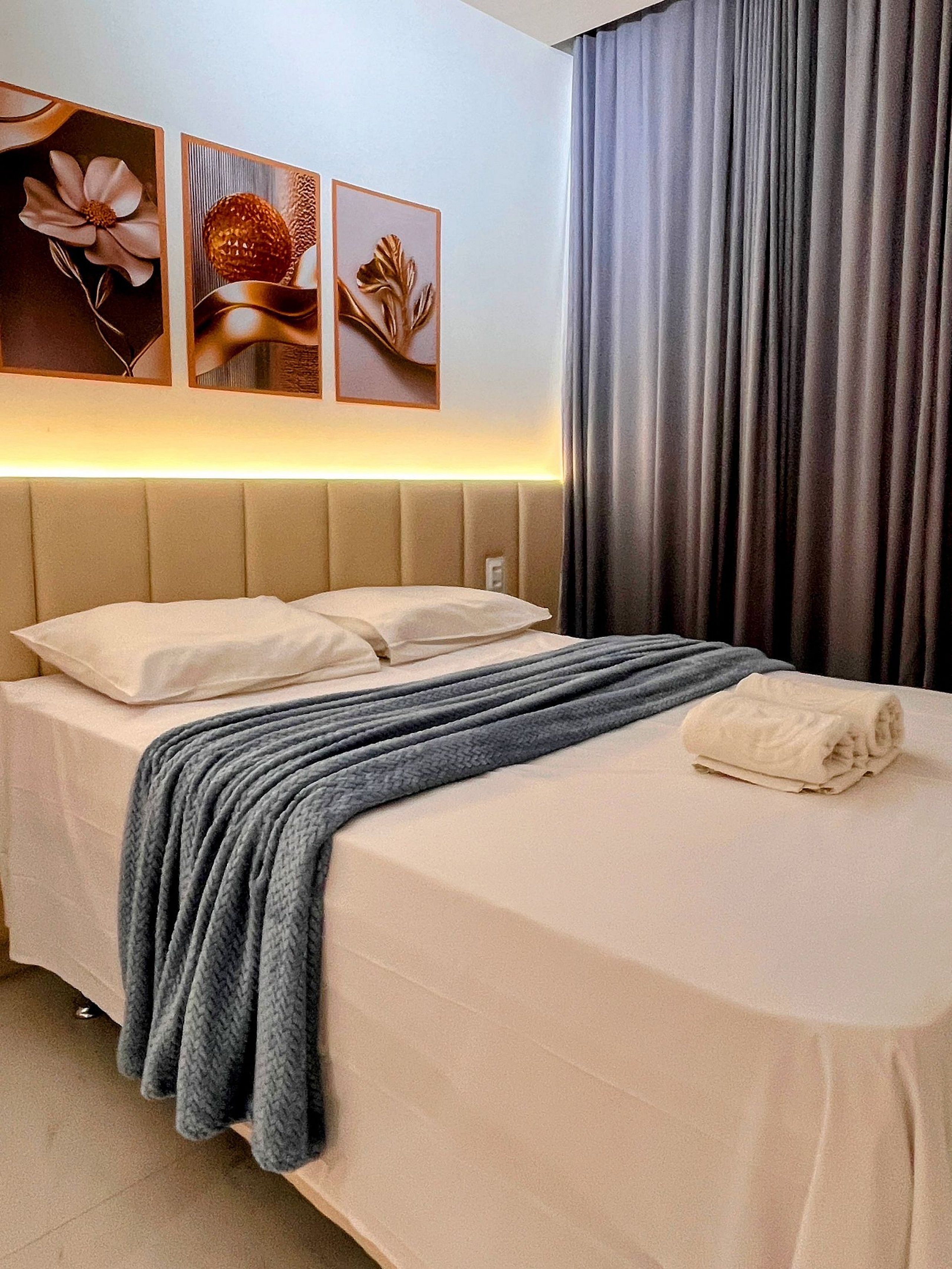 Een hotelkamer met een bed, hoofdeinde, deken, kussen en een muur met ingelijste kunstwerken.