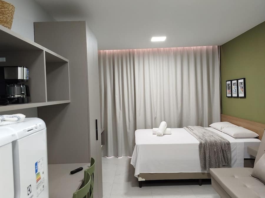 Una habitación de hotel con una cama, un escritorio, una silla, una cafetera y una pared verde.