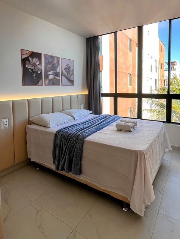 Una camera d'albergo con un letto, una testiera, una finestra con tende e opere d'arte appese al muro.