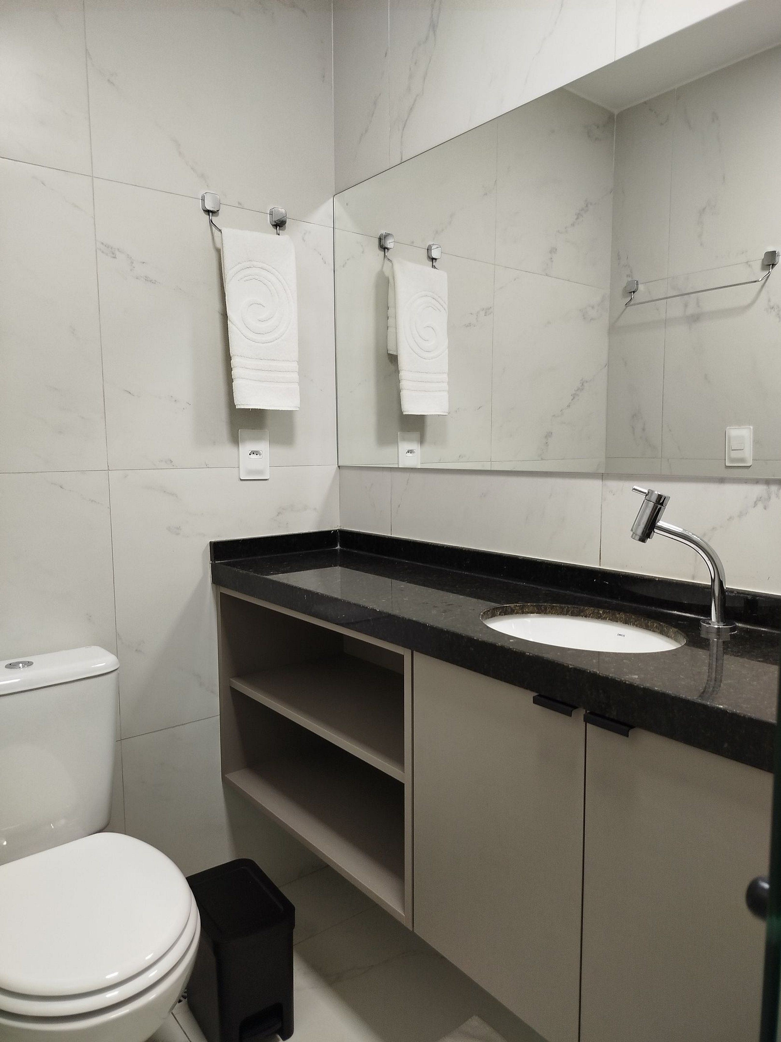 Een moderne badkamer met een wit toilet, een zwart aanrechtbakje en een grote spiegel.