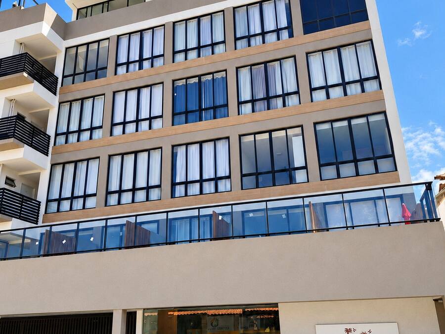 A multi-story hotel with a modern design, featuring a ground-level entrance, a visible parking area, and a sign indicating the hotel's name.