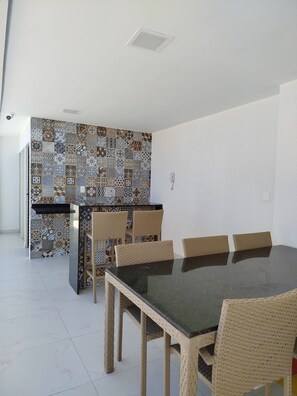 A dining area with a black table and wicker chairs, a patterned backsplash, and a white wall. - Porto City - Porto de Galinhas (Ipojuca)