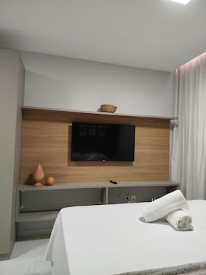 A modern hotel room with a flat-screen TV mounted on a wooden panel above a gray console table. - Porto City - Porto de Galinhas (Ipojuca)