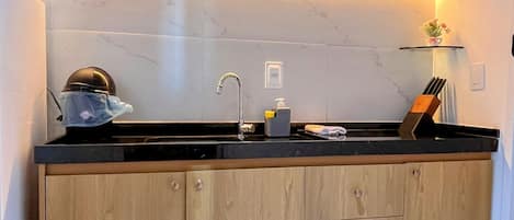 A kitchen with wooden cabinets, a black countertop, a sink, and a small shelf with items.