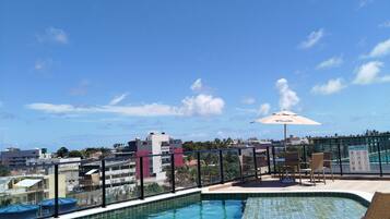 Uma piscina no terraço com águas azul-claras, rodeada por espreguiçadeiras e um guarda-sol.
