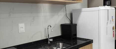 A kitchen with a black countertop, a white microwave, a white refrigerator, and a wooden shelf above the counter.