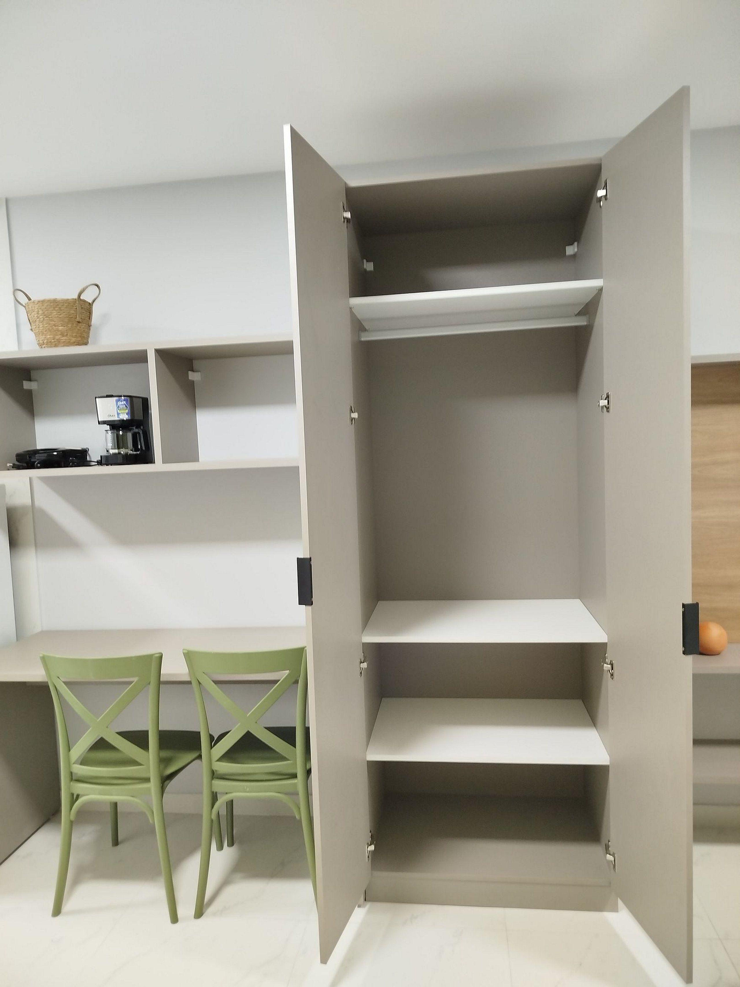 Una habitación con armario empotrado, cafetera, cesta y dos sillas verdes.