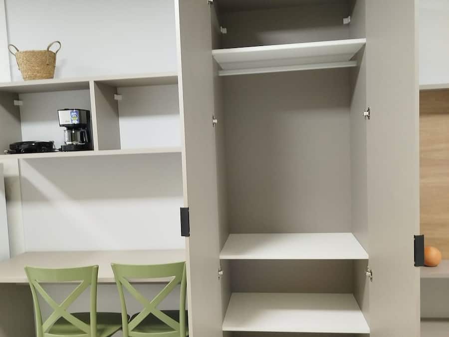 Ein Zimmer mit Einbauschrank, Kaffeemaschine, Korb und zwei grünen Stühlen.