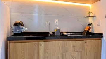 A kitchen with wooden cabinets, a black countertop, a sink, and a small shelf with items.