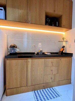 A kitchen with wooden cabinets, a black countertop, a sink, and a small shelf with items. - Porto City - Porto de Galinhas (Ipojuca)