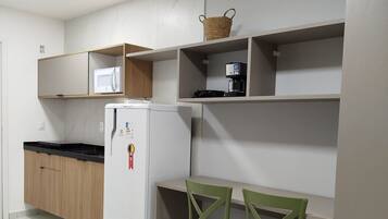 Uma cozinha compacta com geladeira, micro-ondas e cafeteira nas prateleiras, e uma mesa pequena com duas cadeiras.